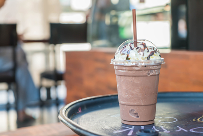 Mrożone frappe czekoladowe w plastikowym kubku z bitą śmietaną na stoliku